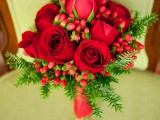 a bold Christmas wedding bouquet of red roses, fir branches and red berries is a bright and cool idea to rock