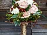 an elegant rustic Christmas wedding bouquet of blush roses, greenery, berries, twigs and with a gold wrap for more chic