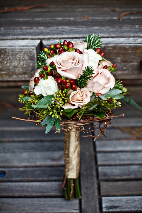 an elegant rustic Christmas wedding bouquet of blush roses, greenery, berries, twigs and with a gold wrap for more chic