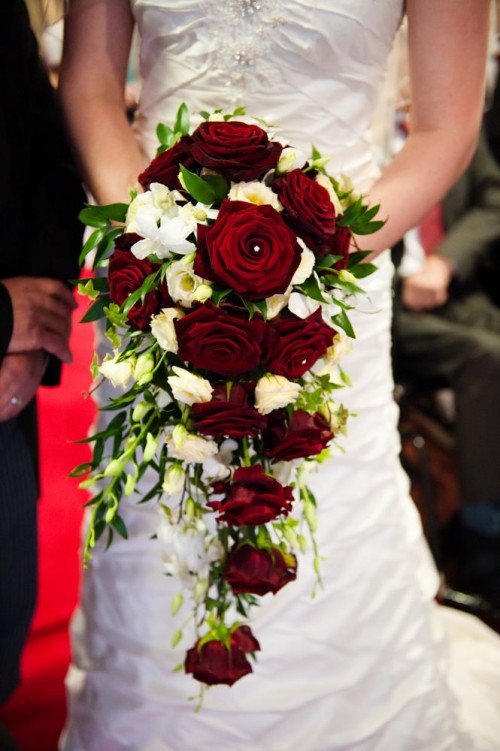 a cascading Christmas wedding bouquet of white and burgundy roses, greenery and some rhinestones is amazing