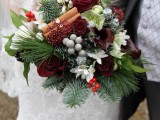 a unique Christmas wedding bouquet of white and burgundy blooms, berries, leaves and greenery plus cinnamon sticks