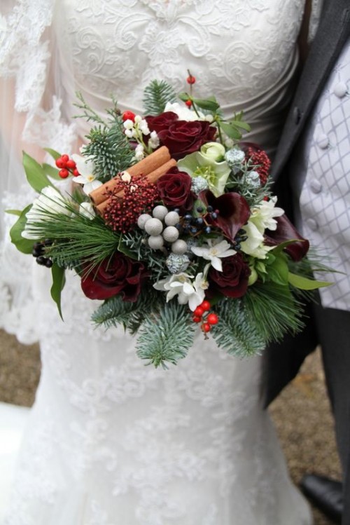 a unique Christmas wedding bouquet of white and burgundy blooms, berries, leaves and greenery plus cinnamon sticks