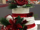 a Christmas wedding cake decorated with red ribbons, cranberries, pinecones, faux greenery and blooms is a cozy rustic piece