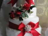 a white wedding cake with a snowflake tier, red ribbon bows with embellishments, greenery and faux roses is a pretty and bold dessert