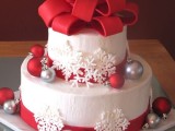 a white Christmas wedding cake decorated with red and silver ornaments, white snowflakes and with a large red bow on top looks very holiday-like