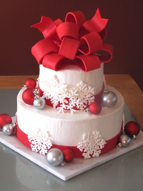 A white Christmas wedding cake decorated with red and silver ornaments, white snowflakes and with a large red bow on top looks very holiday like