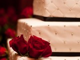 a refined Christmas wedding cake in white decorated with black ribbons and beads plus red roses is a cool idea for Christmas