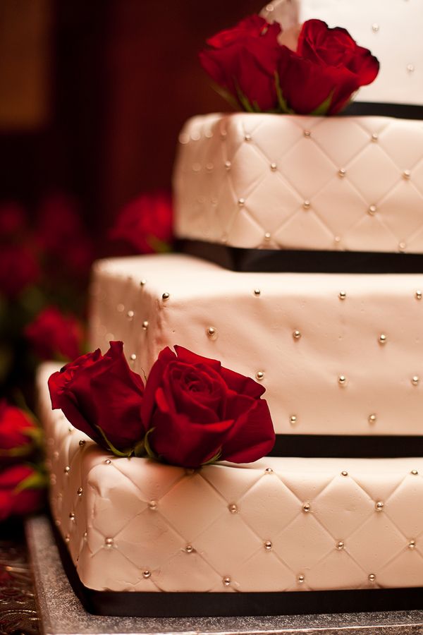 A refined Christmas wedding cake in white decorated with black ribbons and beads plus red roses is a cool idea for Christmas