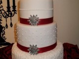a white Christmas wedding cake decorated with red ribbons, embellishments and with textural layers plus a glam topper