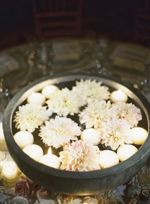 a stone bowl with floating white blooms and candles is a chic and pretty decoration for both indoors and outdoors