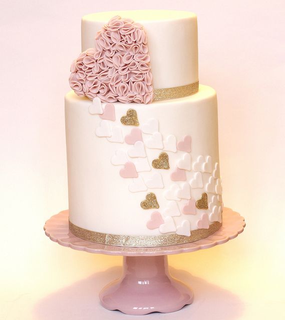 A neutral wedding cake with gold stripes, a blush cream hearts and more hearts decorating the cake