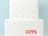 a white square wedding cake decorated with letters and with red LOVE letters for making it bold and fun