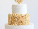a round white and tan wedding cake with plain and sleek and ruffled tiers, some dot patterns and a ruffle heart on top