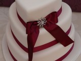 a refined white heart-shaped wedding cake with red ribbons and a bow with embellishments is a stylish and beautiful idea