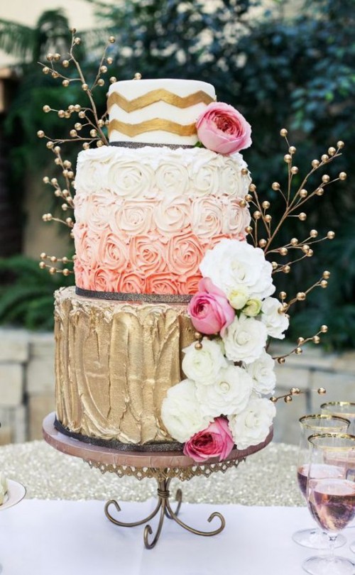 a whimsical wedding cake with gold, ombre pink and a chevron one, decorated with fresh blooms, gilded berries on branches is a beautiful dessert