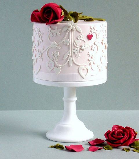 a light pink and white wedding cake with patterns, a tiny red heart and red roses on top is a lovely idea