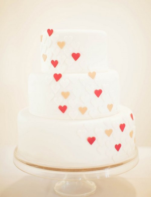 a white wedding cake decorated with red and pink hearts is a lovely and bright idea for a Valentine wedding
