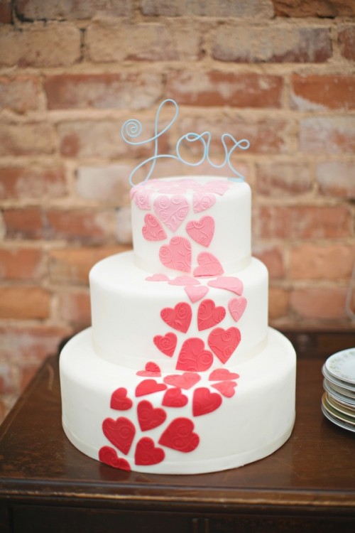 a modern and bold white wedding cake decorated with ombre hearts and a wire topper is a lovely and bold idea