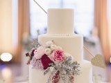 a beautiful Valentine wedding cake in white, with bold blooms and pale greenery plus an arrow with gold glitter feels very Valentine-like