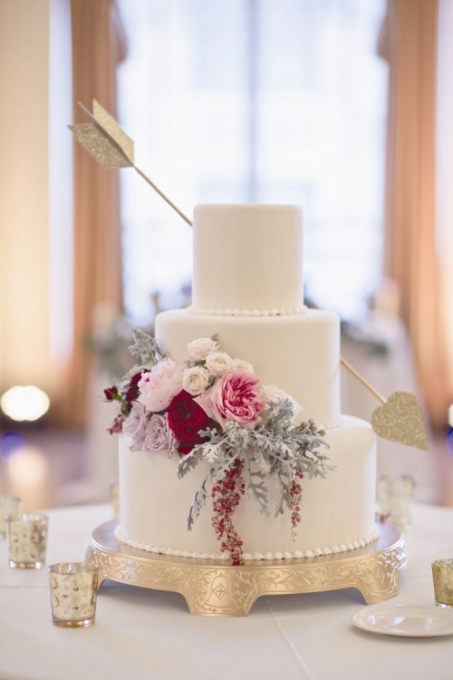 a beautiful Valentine wedding cake in white, with bold blooms and pale greenery plus an arrow with gold glitter feels very Valentine-like