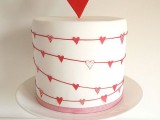 a white wedding cake decorated with garlands of pink, red and silver glitter hearts and with a heart topper is great for Valentine’s Day