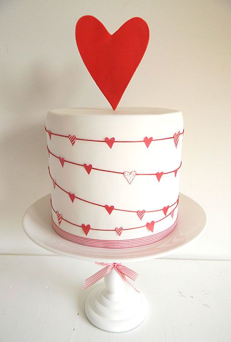 a white wedding cake decorated with garlands of pink, red and silver glitter hearts and with a heart topper is great for Valentine's Day