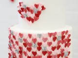 a white wedding cake decorated with pink, grey and red hearts – they cover the lower tier and form a heart on the upper one