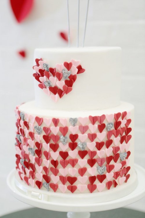 a white wedding cake decorated with pink, grey and red hearts - they cover the lower tier and form a heart on the upper one