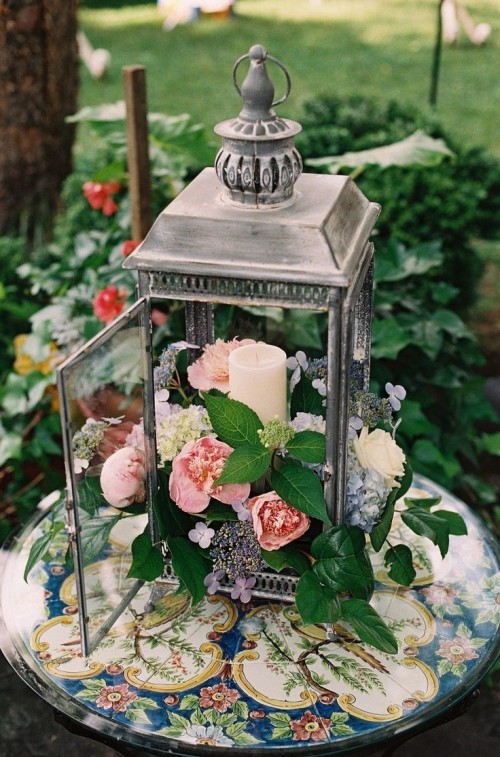 a stylish vineyard wedding centerpiece - a candle lantern filled with pink and coral blooms and greenery