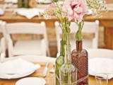 tied up wine bottles with greenery, pink flowers and baby’s breath plus a wood slice table number