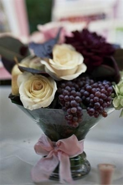 a lush vineyard wedding centerpiece of white and deep purple blooms and grapes is a nice idea to go for