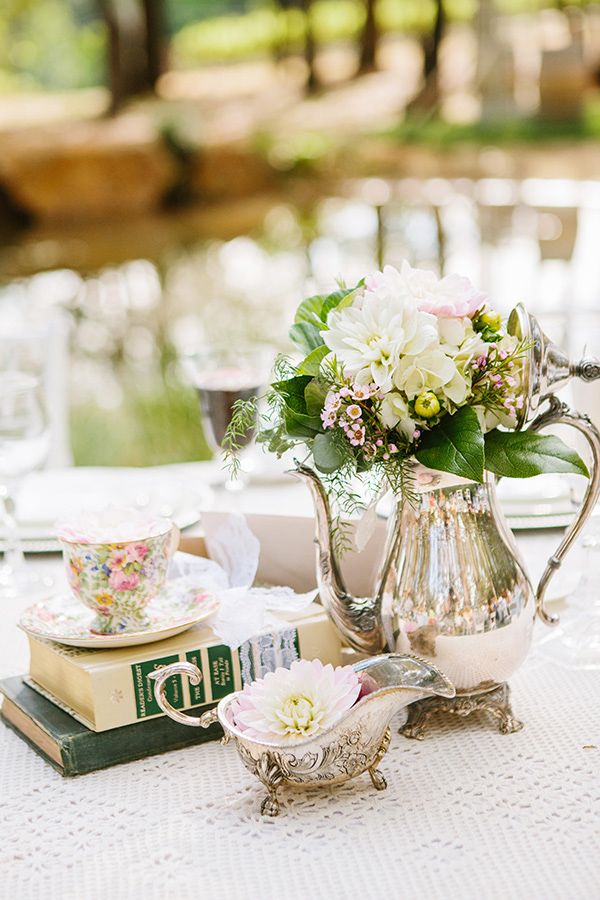 An elegant vintage wedding centerpiece of a silver tea pot and milker, neutral blooms and a floral cup for a vintage vineyard wedding