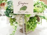 a delicate vineyard wedding centerpiece of a vintage urn, neutral blooms, grapes and leaves plus a table name