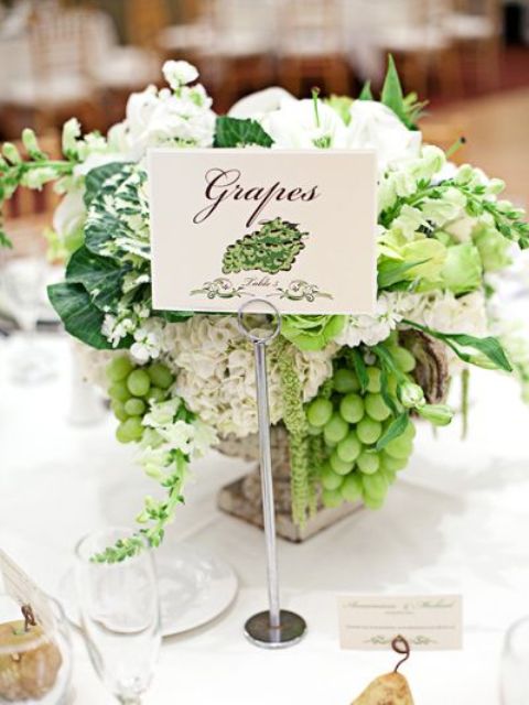 a delicate vineyard wedding centerpiece of a vintage urn, neutral blooms, grapes and leaves plus a table name