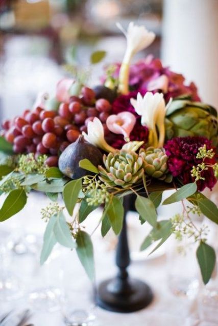 a bright vineyard wedding centerpiece of greenery, neutral blooms, grapes and figs is perfect for fall