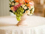 a chic vintage vineyard wedding centerpiece of a pink urn, some red and pink blooms and grapes cascading down