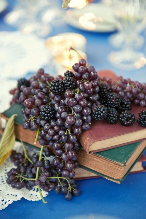 a vintage vineyard wedding centerpiece of a stack of books, grapes and blackberries looks lush and very decadent