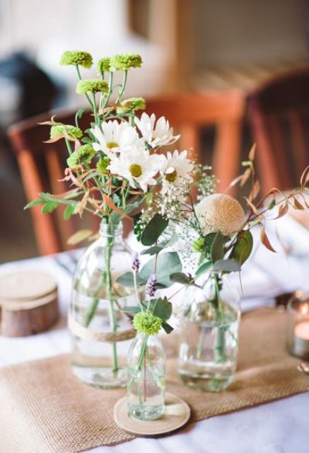 a simple vineyard wedding centerpiece of glass bottles and jars with greenery and wildflowers will also fit a boho or rustic wedding