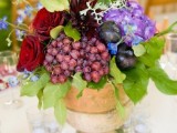 a vineyard wedding centerpiece  of a vintage urn, bright burgundy and purple flowers, grapes and plums for a fall vineyard wedding