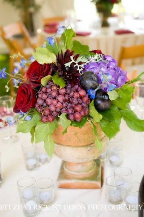 a vineyard wedding centerpiece  of a vintage urn, bright burgundy and purple flowers, grapes and plums for a fall vineyard wedding
