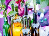 a bright vineyard wedding centerpiece of various wine bottles and some blooms and greenery for a modern wedding