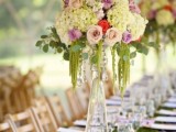 a tall clear glass vase with neutral and bright blooms and cascading greenery is a cool idea for a centerpiece