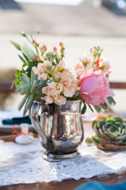a silver tea pot with blush, pink blooms and greenery is a nice and bold wedding centerpiece for a vineyard celebration