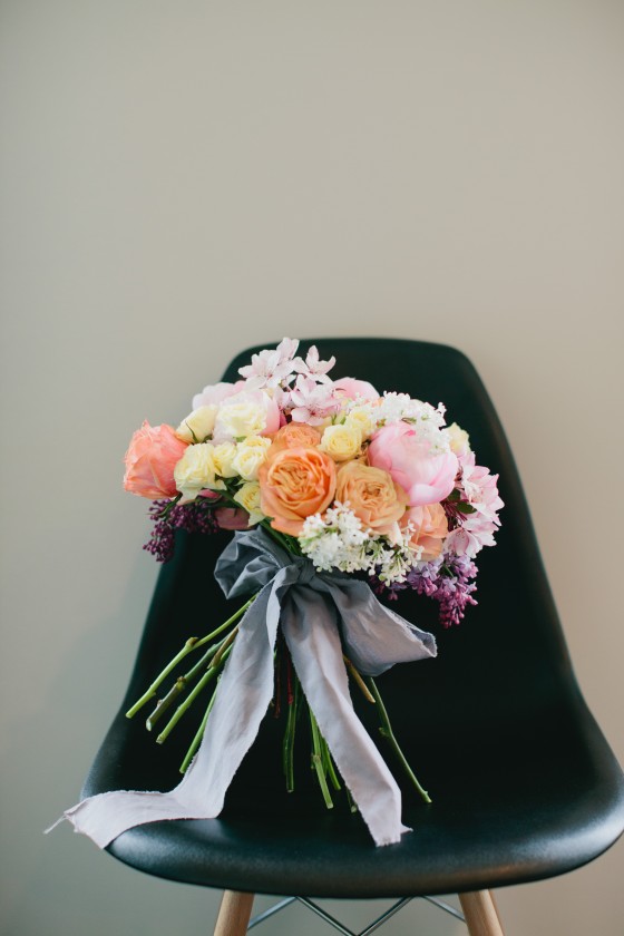 a bright spring wedding bouquet with blush, orange and yellow blooms and grey ribbons