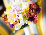 a colorful spring wedding bouquet with yellow, pink, red and blue blooms and some greenery