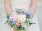 a romantic pastel wedding bouquet with light blue, pink and white blooms and some greenery