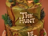 a bright wedding cake with sugar leaves, trees, a deer and a hunter on top hinting on a funny joke