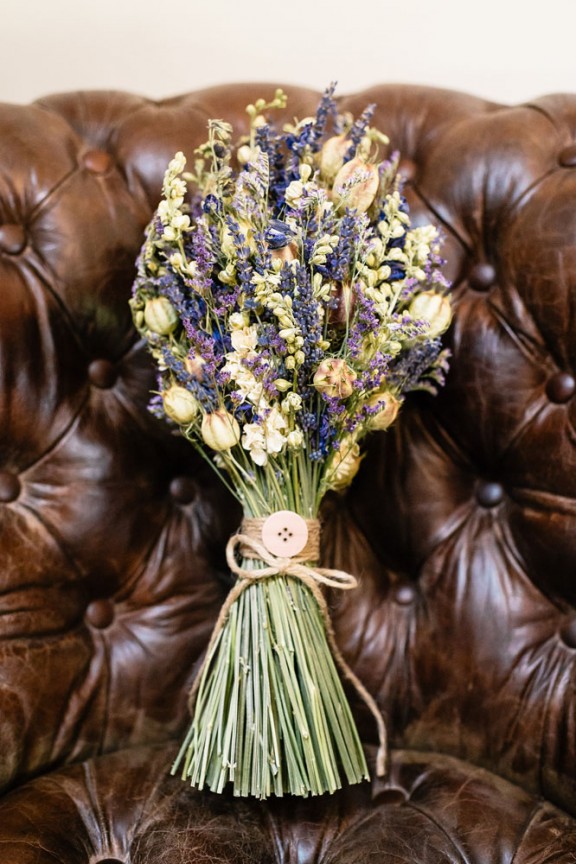 A wedding bouquet of dried blooms and grasses with yarn and a large button is a lovely idea for a summer or summer to fall wedding