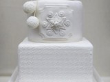a white wedding cake with round and square tiers, with beautiful snowflakes of sugar and some lovely pompoms to feel as cozy as possible