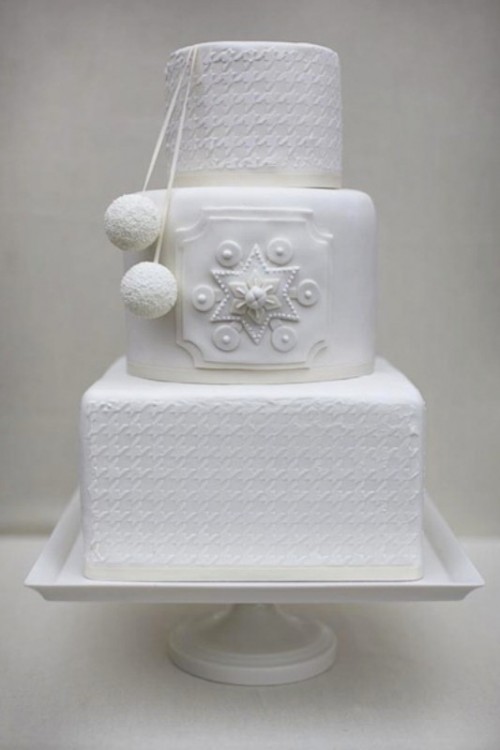a white wedding cake with round and square tiers, with beautiful snowflakes of sugar and some lovely pompoms to feel as cozy as possible